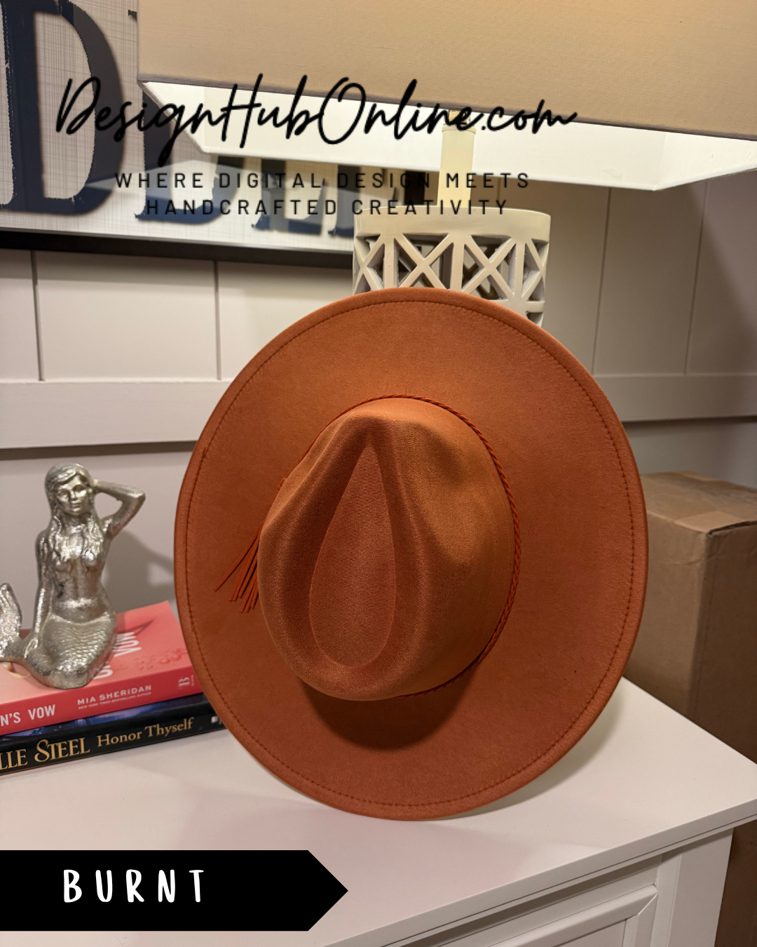 a brown fedora hat placed on a white surface, with a small statue of a mermaid to the left.