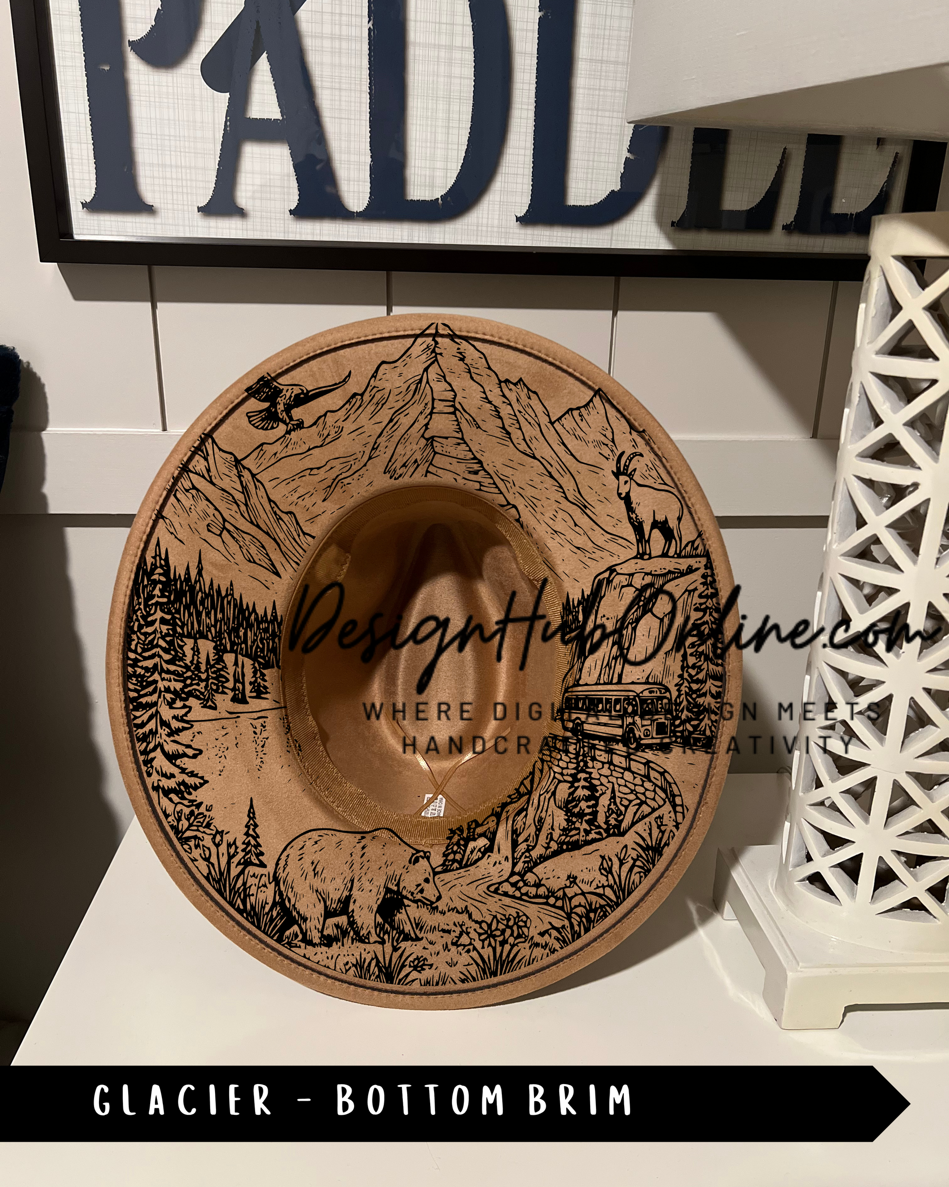 A wooden hat with a mountain landscape design, featuring a bear and other wildlife, is displayed on a shelf.