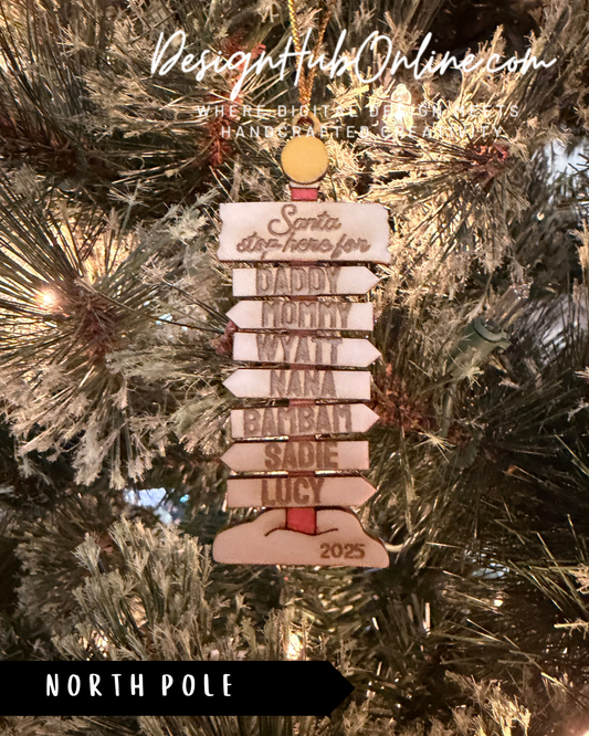 A Christmas ornament with a directional sign hanging on a tree, displaying the names of various relatives or family members.