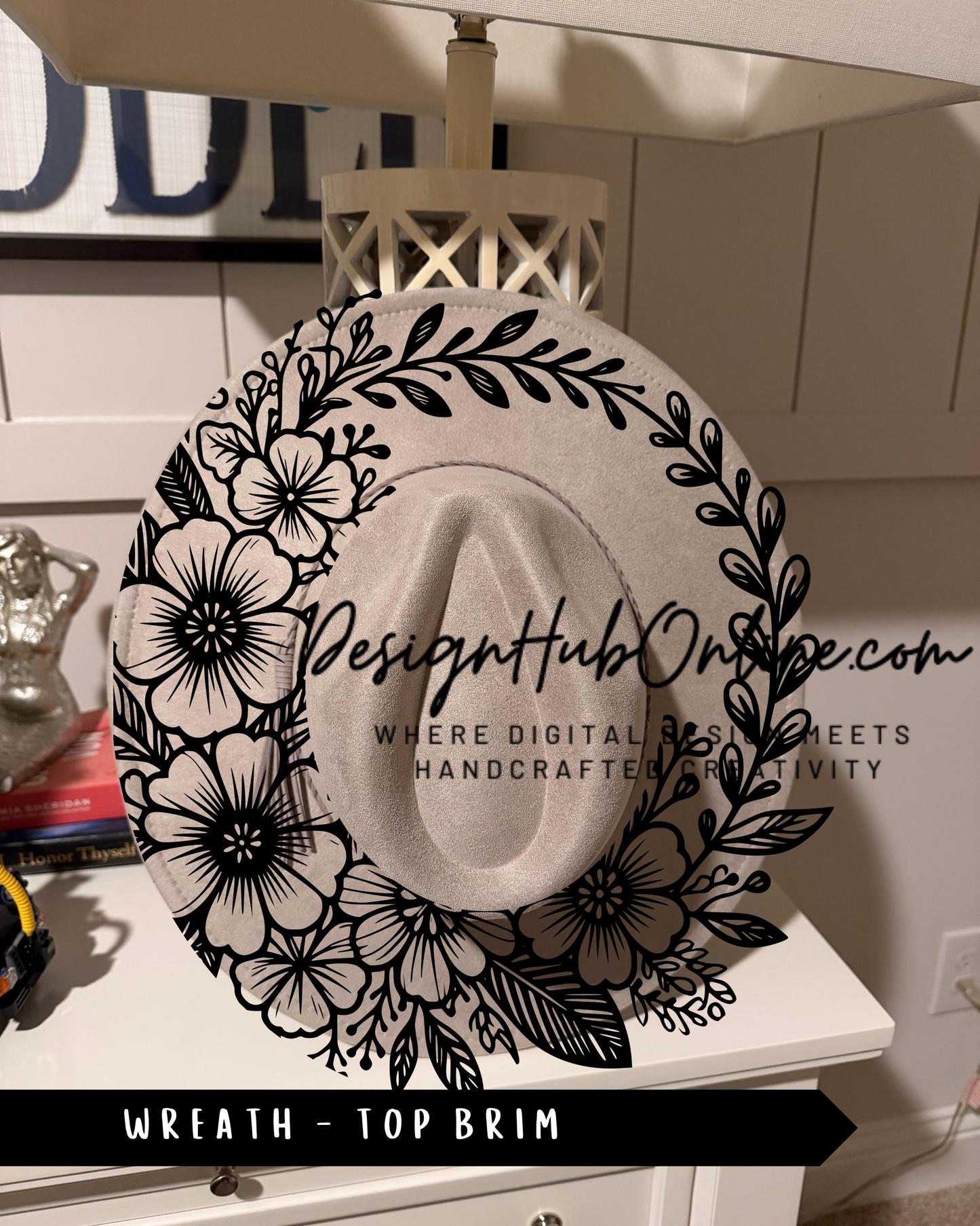 A decorative white hat with a floral design, hanging on a white shelf.