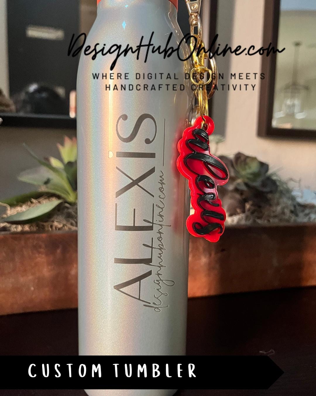A silver tumbler with a red and black keychain charm attached to it, placed on a table.