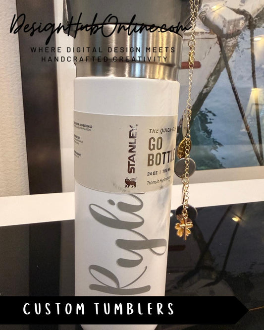 A white and silver Stanley tumbler with a personalized name label, placed on a reflective surface.