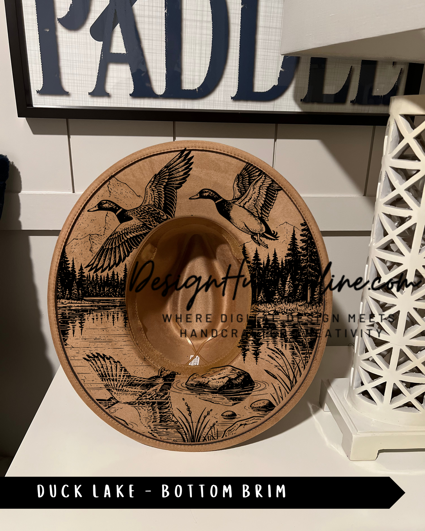 A wooden hat with a design depicting ducks and a lake, placed on a white surface.
