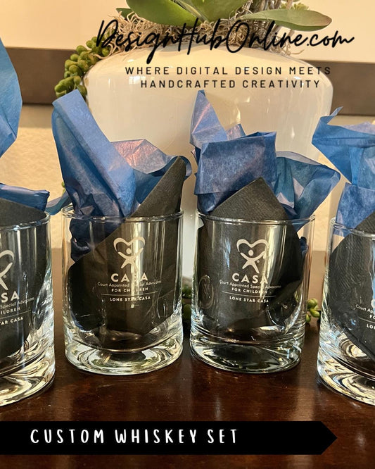 A set of four custom whiskey glasses with blue and black napkins, placed on a wooden surface.