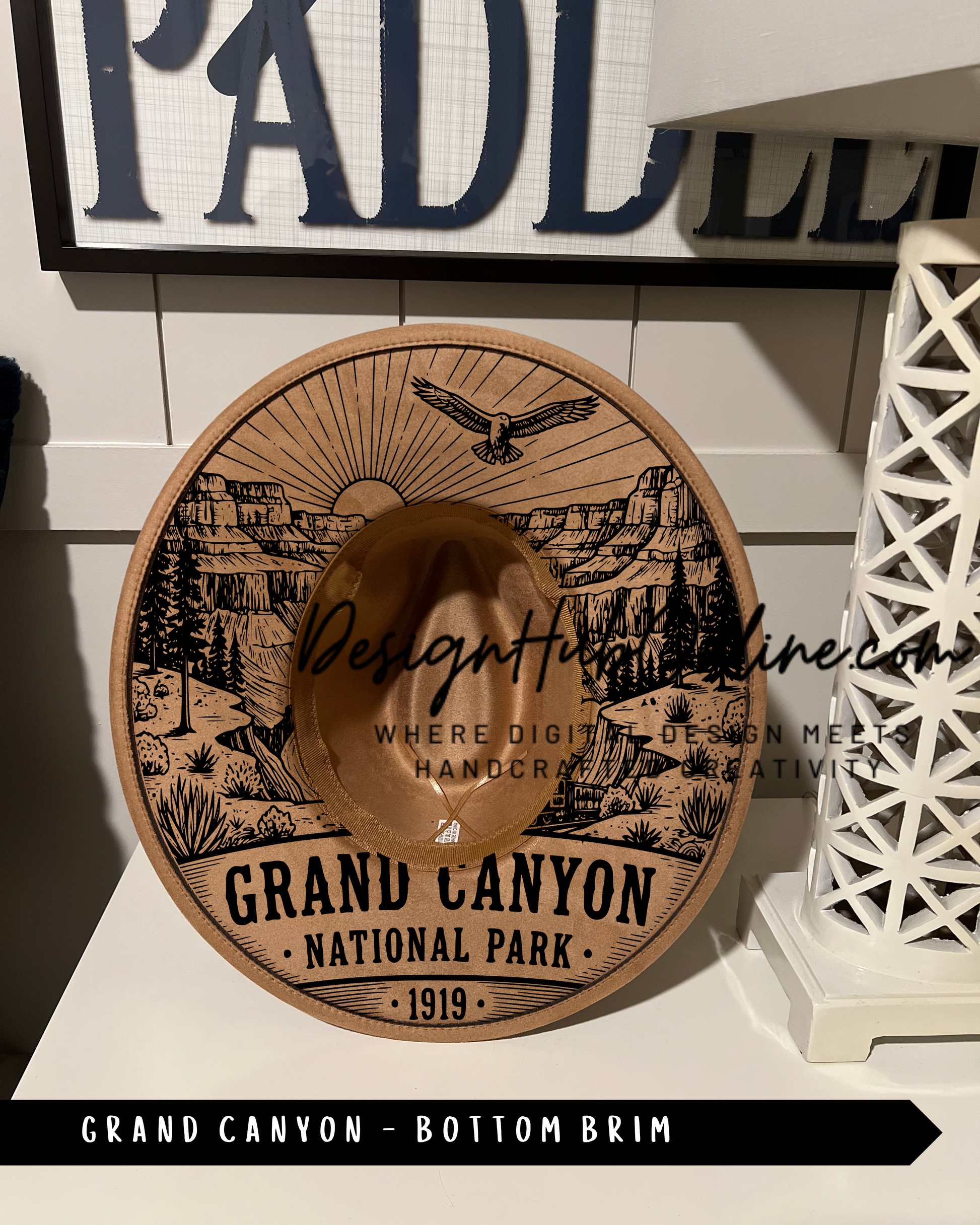 A wooden hat with a printed design of the Grand Canyon National Park, featuring a sun, eagle, and desert landscape.