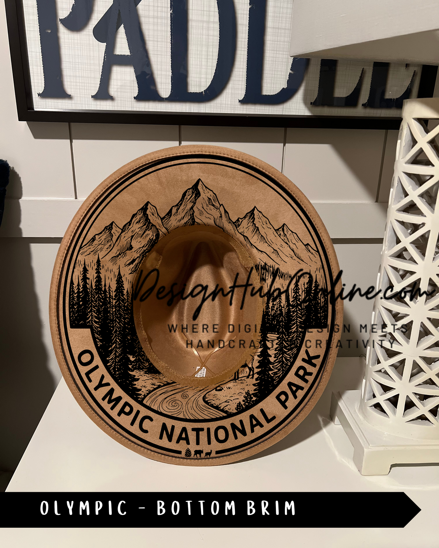 A wooden hat with a mountain landscape design, labeled "Olympic National Park", is displayed on a shelf.