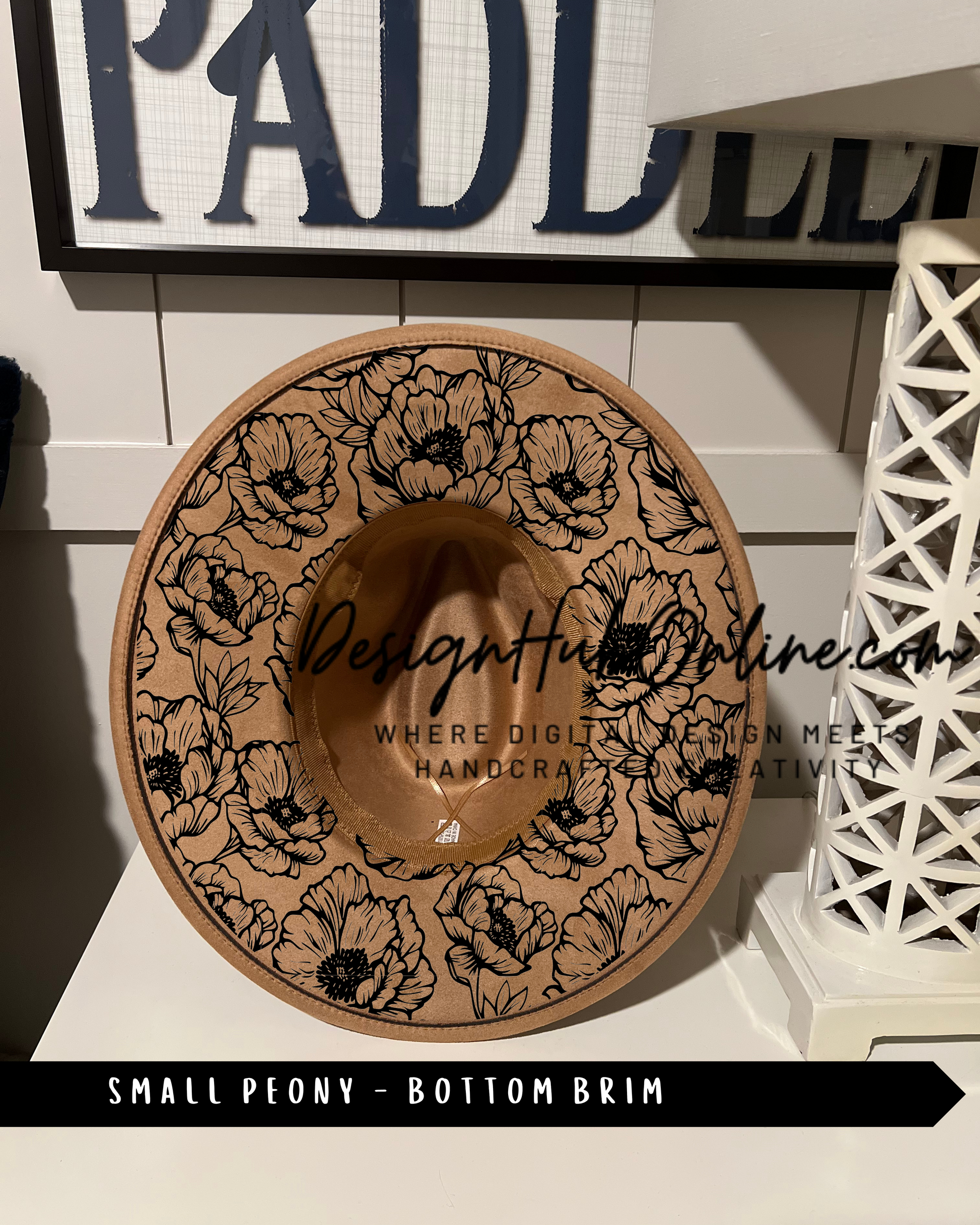 A small peony-patterned hat with a bottom brim design, displayed on a shelf against a white wall with a sign that reads 'PADLL'.