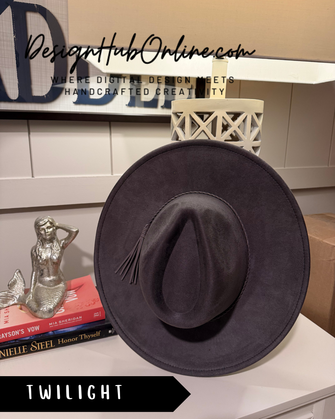 a black cowboy hat placed on a white surface, with a mermaid figurine and some books nearby.