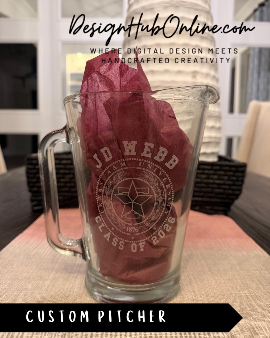 A glass pitcher with a custom design, featuring a star and text, sits on a table.