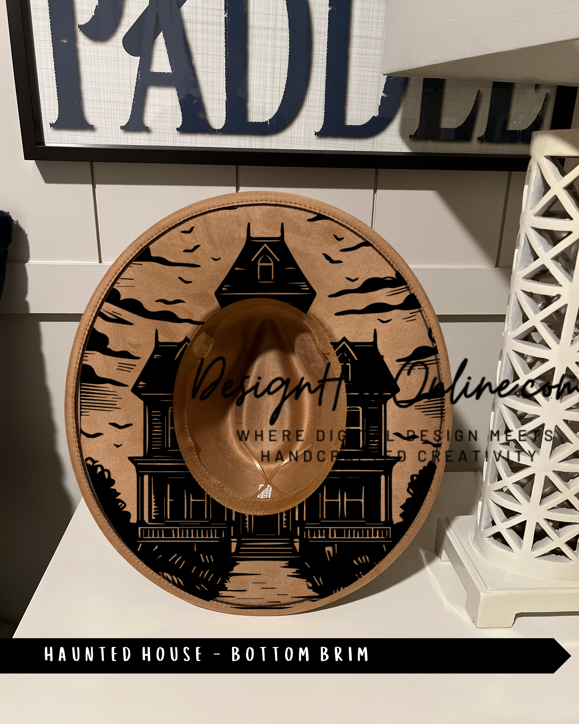 A hat with a house design on it, placed on a shelf next to a white lamp.