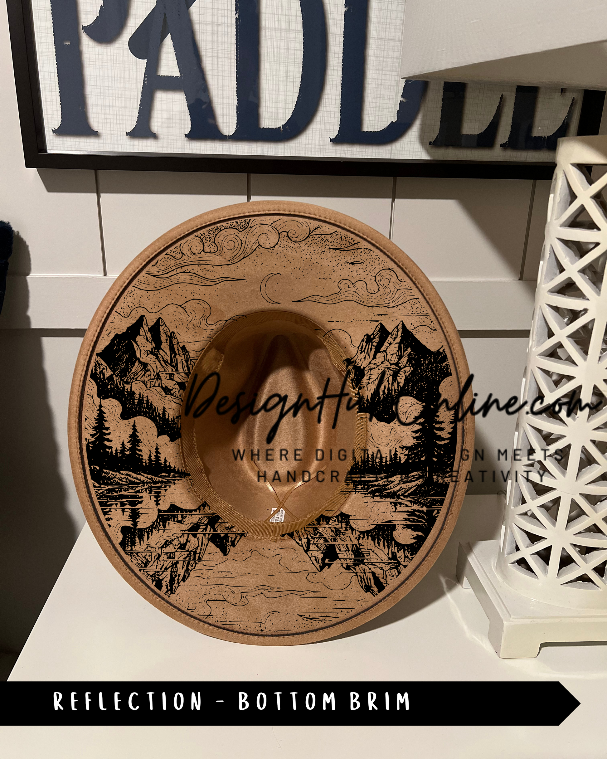 A wooden hat with a mountain landscape design, placed on a white surface.