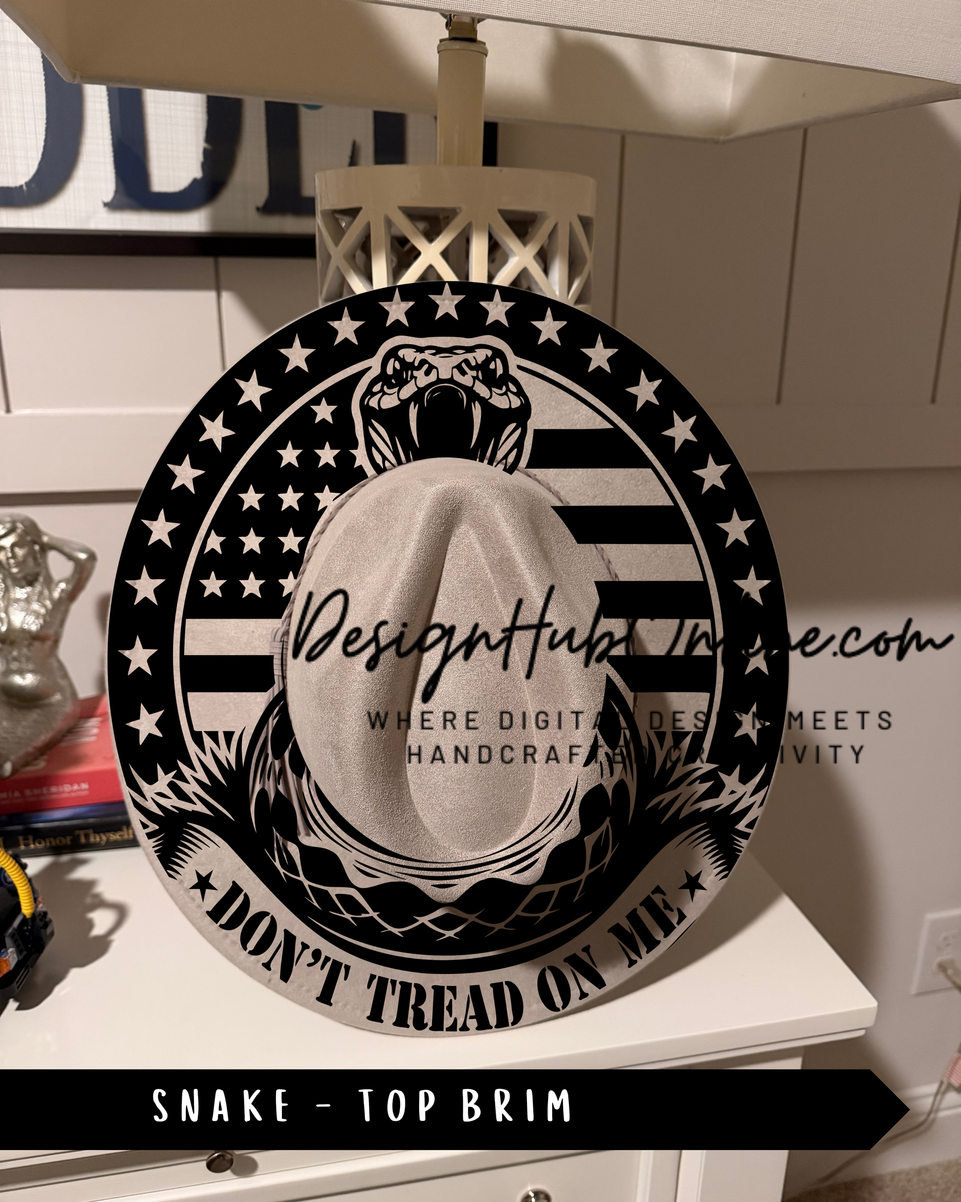 A black and white image of a hat with a snake design, featuring the text "Don't Tread on Me" and "Top Brim" printed on it.