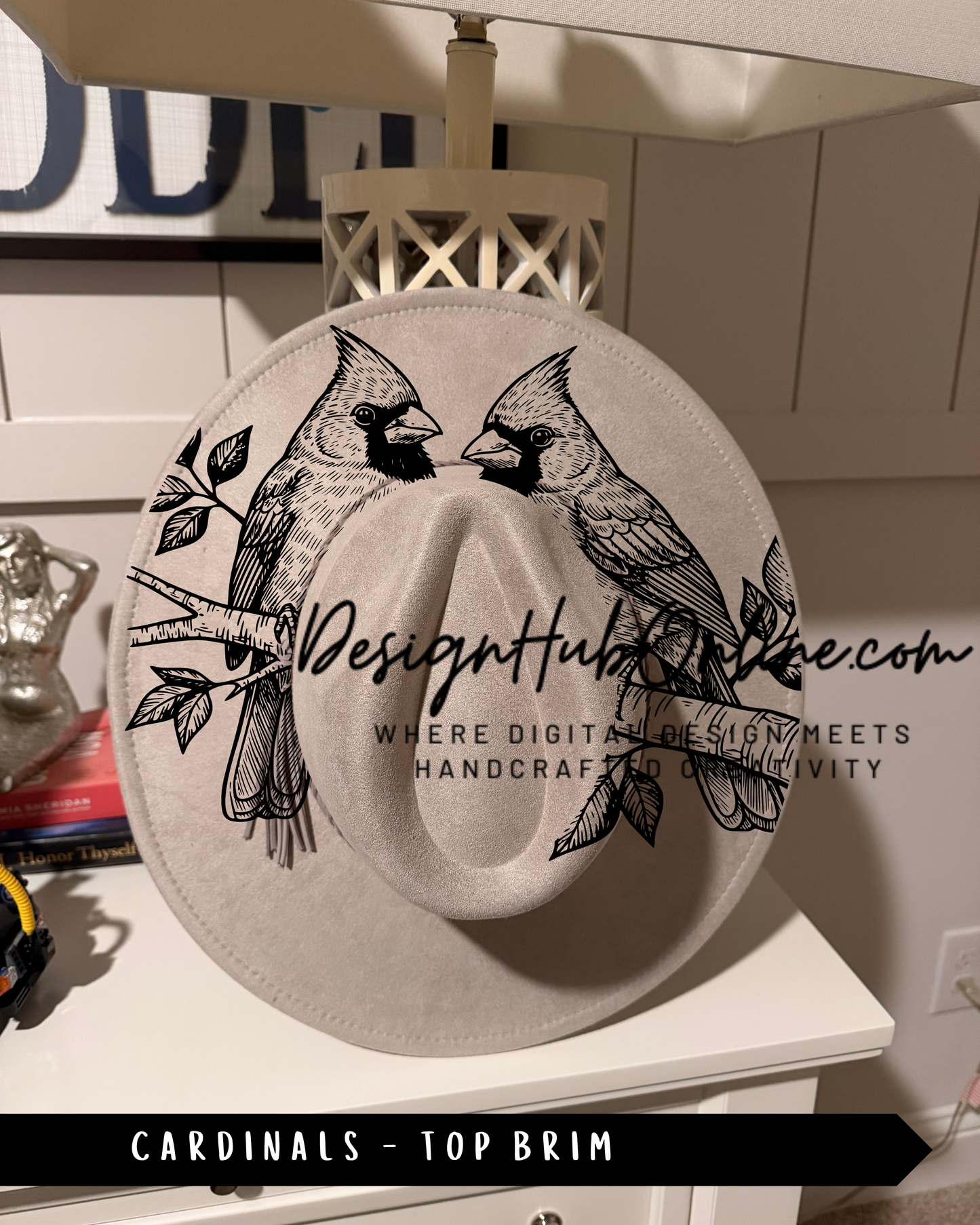 A white hat with a black and white illustration of two cardinals perched on a branch, along with the text "Design Hub" and "Where digital design meets handmade craftsmanship and luxury".