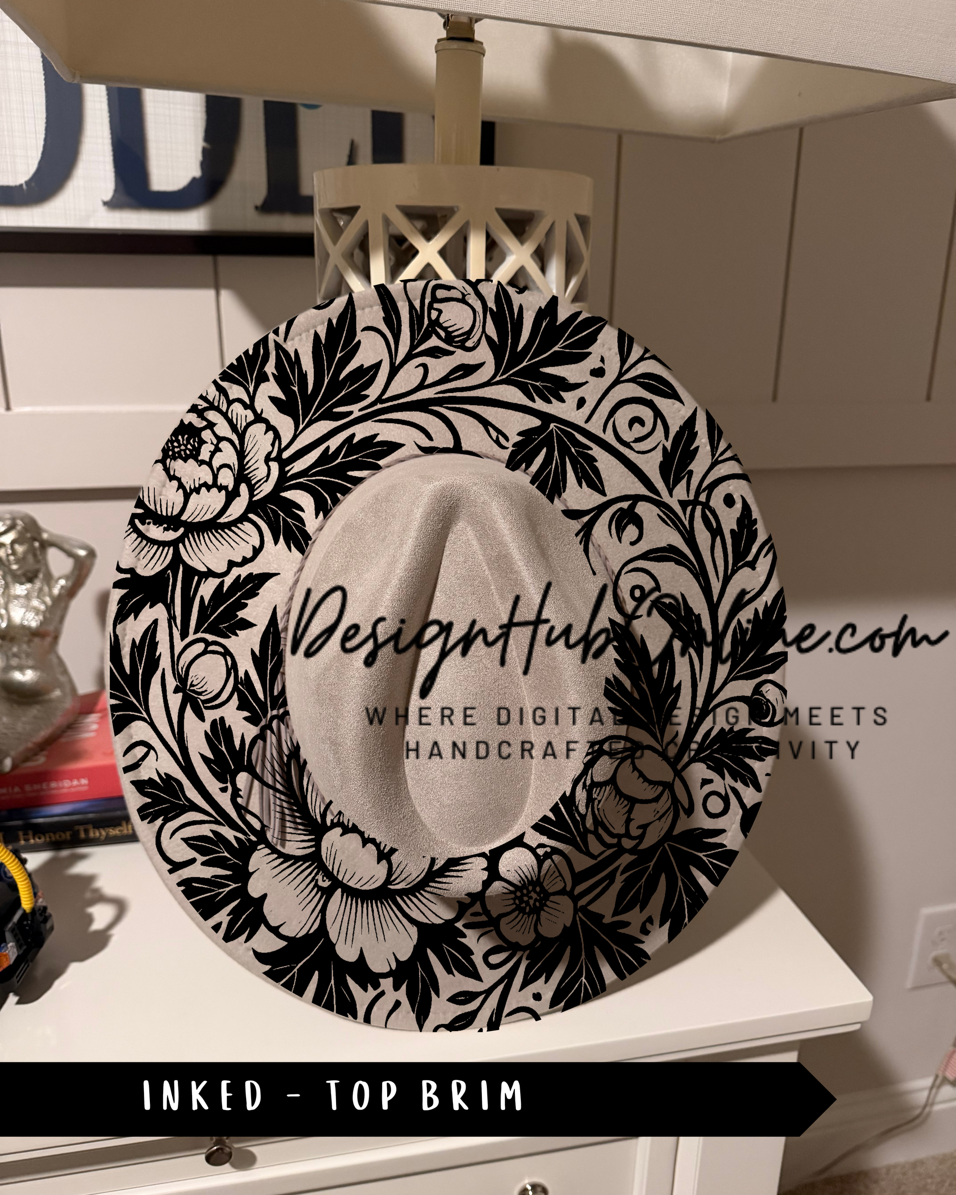 A decorative black and white hat with a floral pattern, sitting on a white surface.