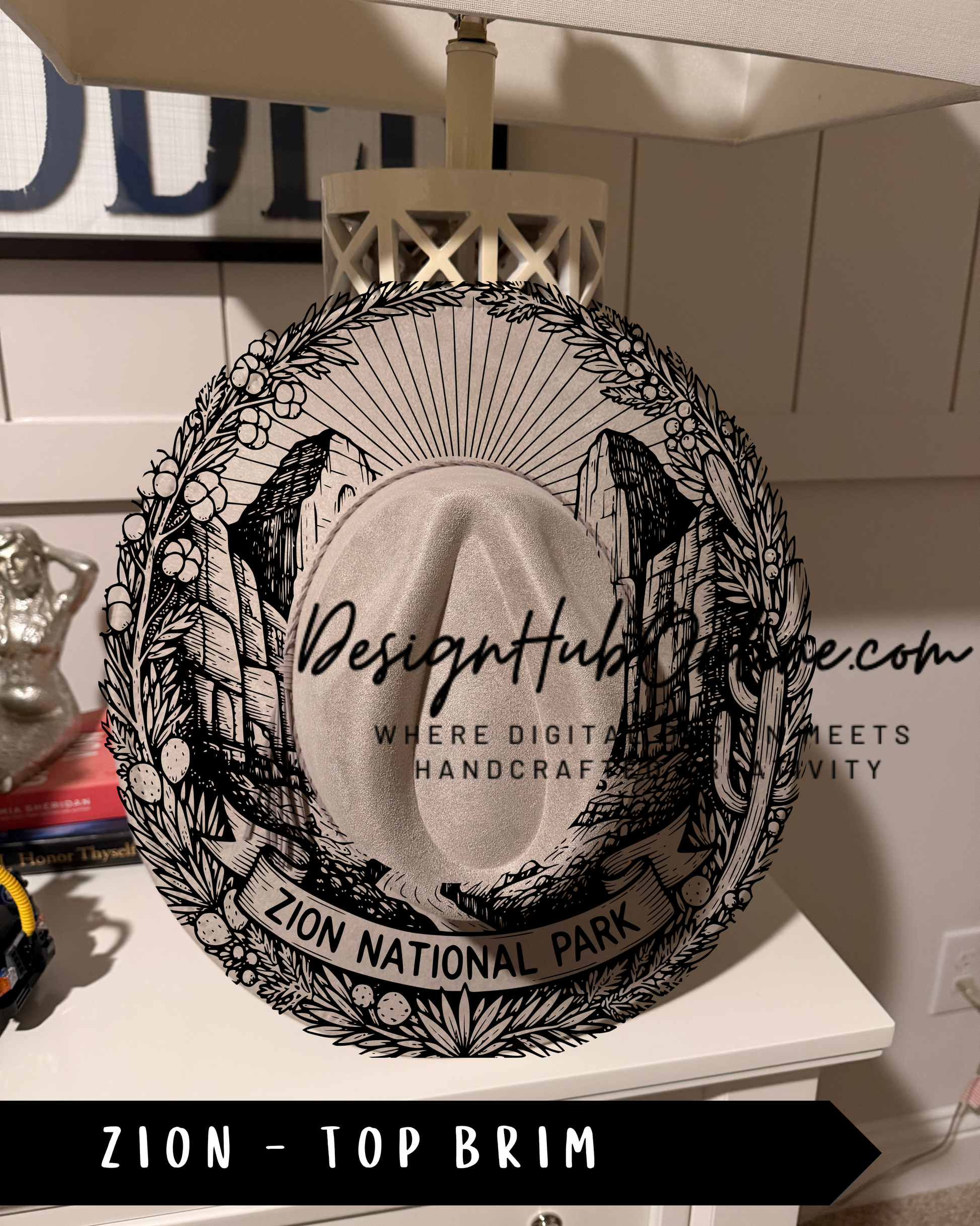 A decorative wall hanging or lampshade with a black and white illustration of a hat and the text "ZION NATIONAL PARK" printed on it.
