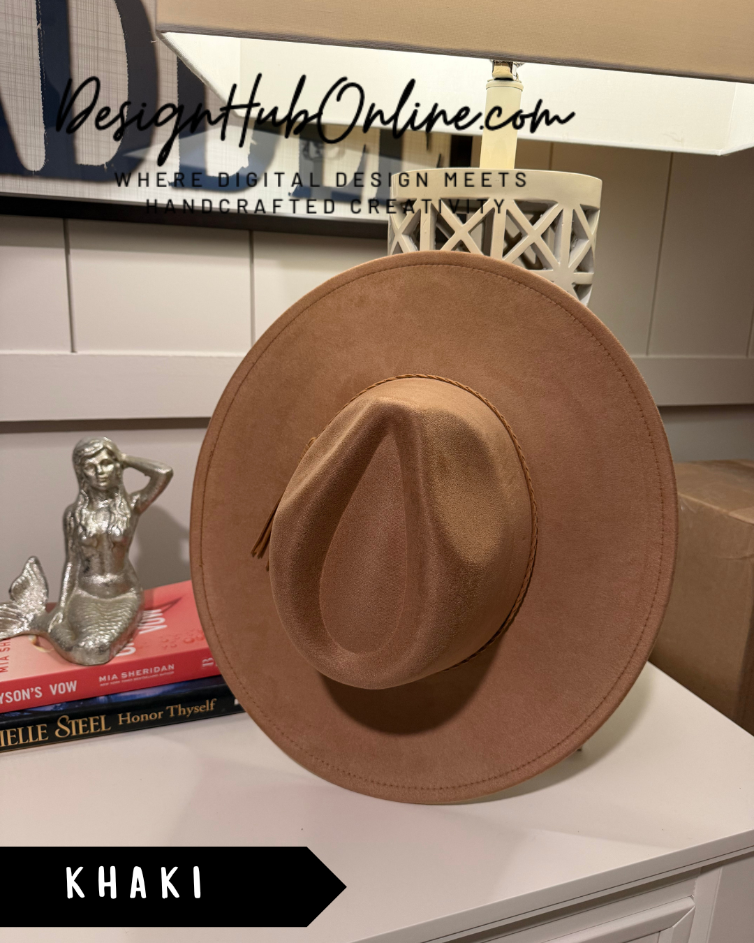 A brown cowboy hat is displayed on a white surface, with a mermaid figurine and a stack of books visible in the background.