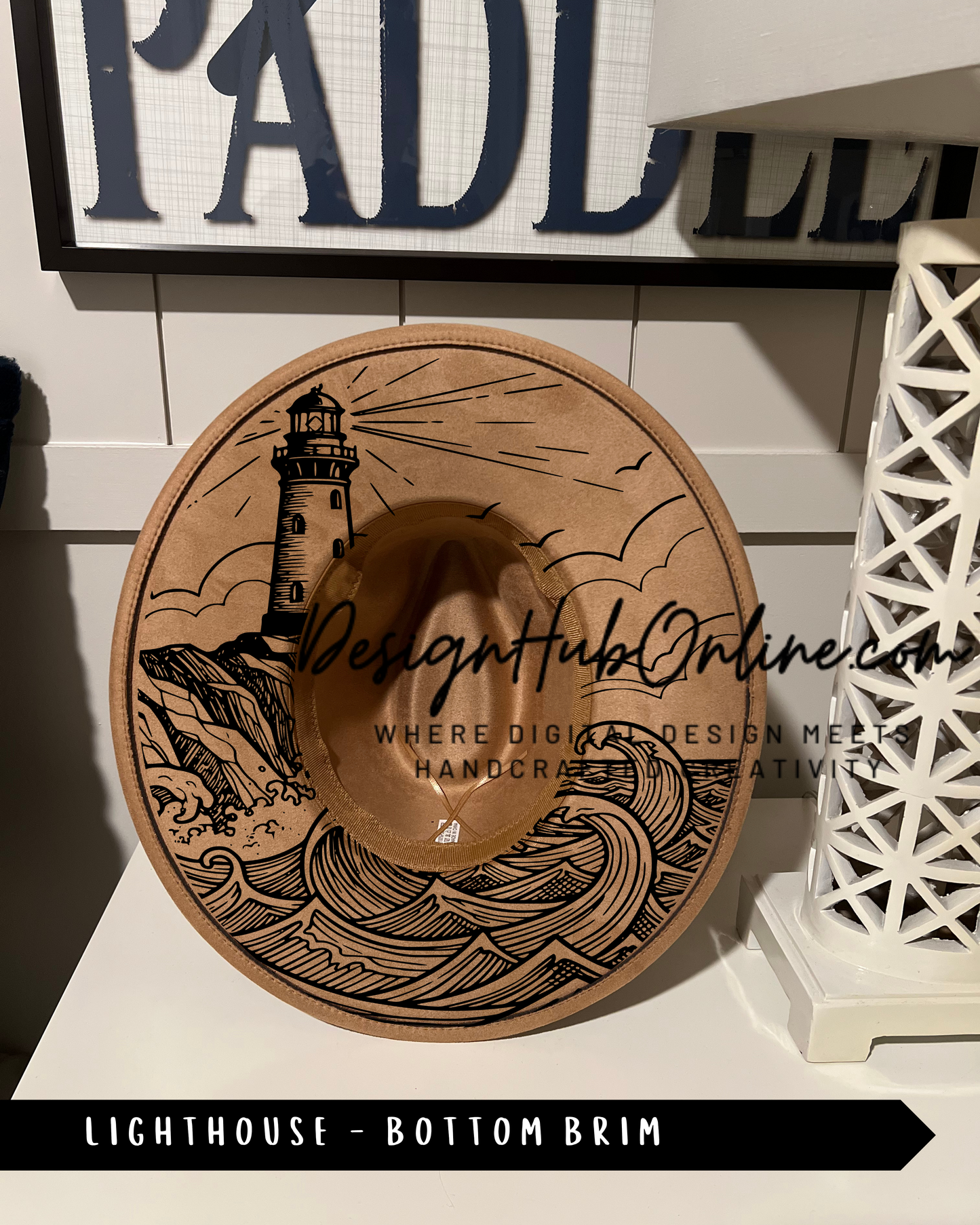 A wooden hat with a lighthouse design on it, placed on a white surface.