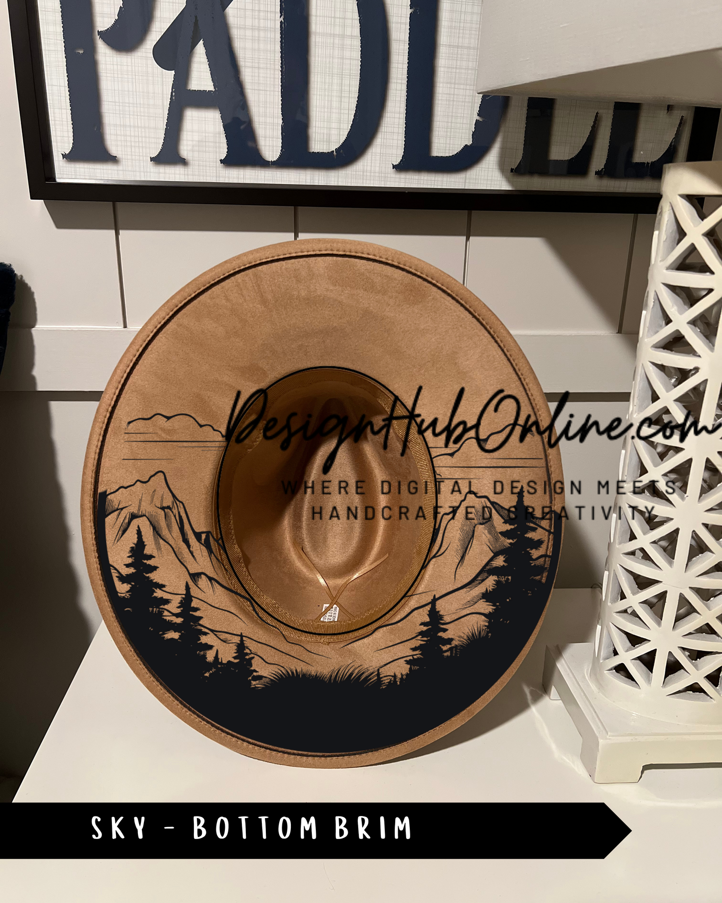 A wooden hat with a mountain landscape design on it, displayed on a white surface.