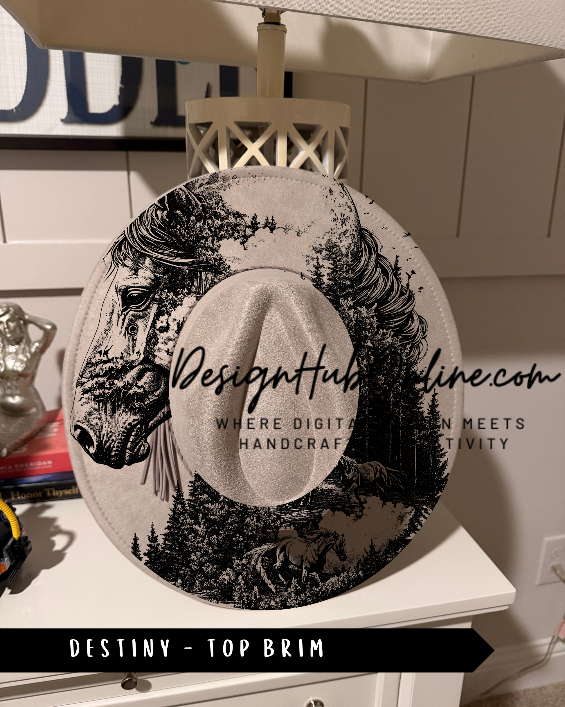 A hat with a black and white illustration of a horse and a forest scene on it, placed on a white dresser.