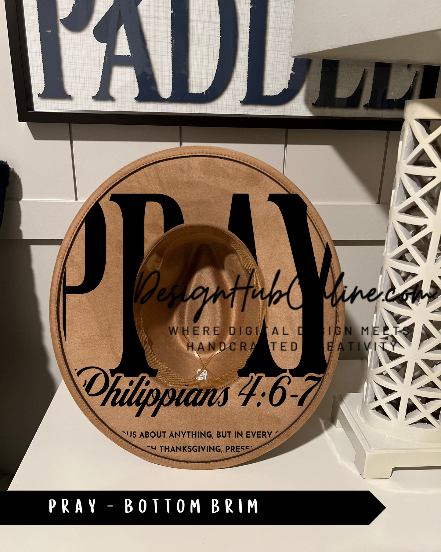 A brown hat with the word "PRAY" printed on it, placed on a white surface.