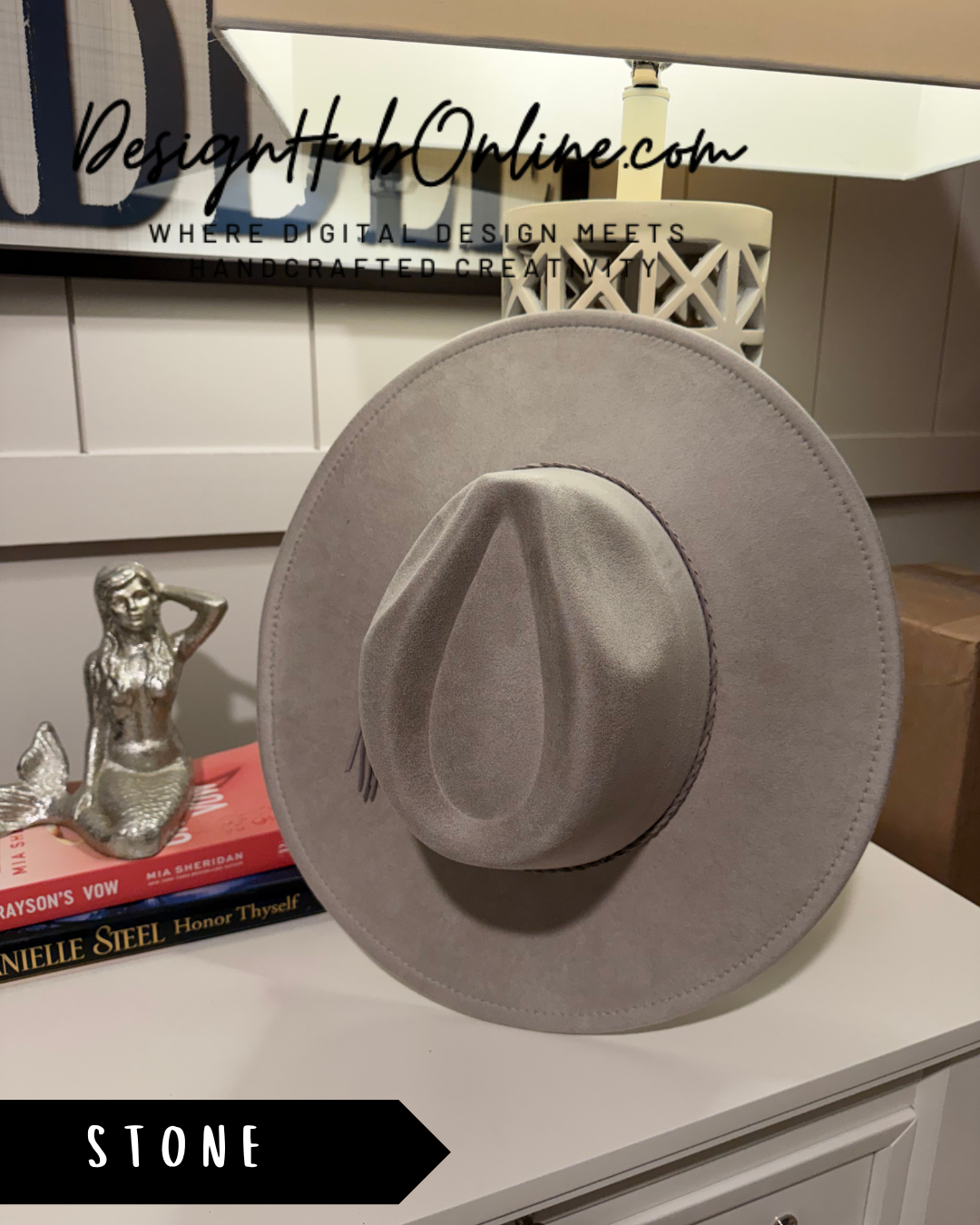 a gray cowboy hat placed on a white dresser, with a small statue of a mermaid to the left.