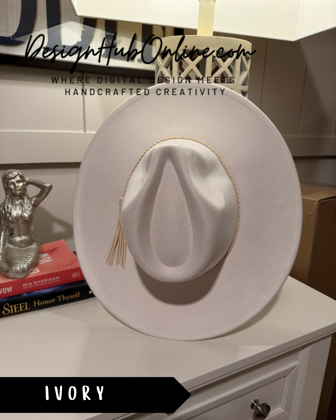 A white cowboy hat with a tassel is displayed on a white dresser, accompanied by a small figurine and a book.